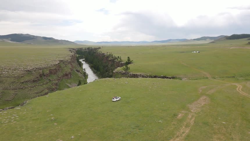 Aerial of a car driving through a meadow in a deserted rural town