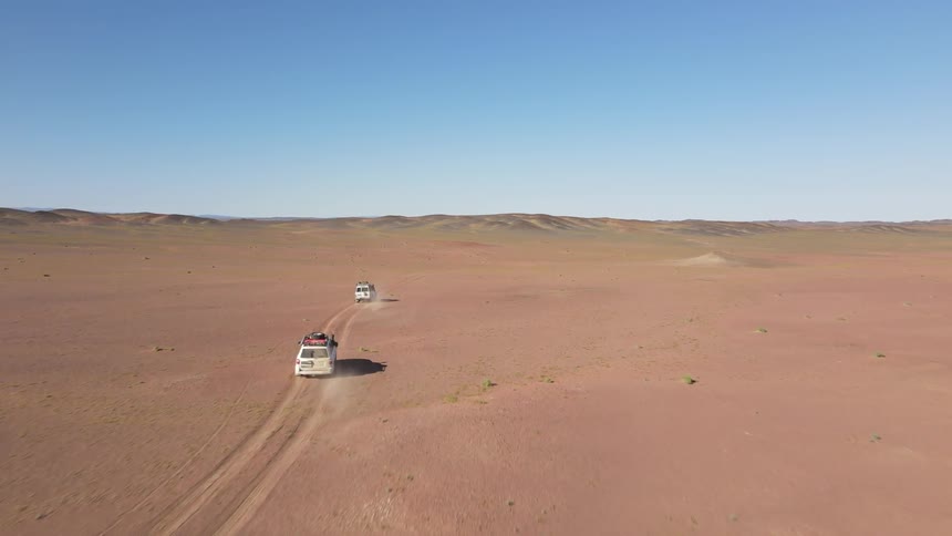 White vehicles driving quickly across a barren desert terrain on a bright day