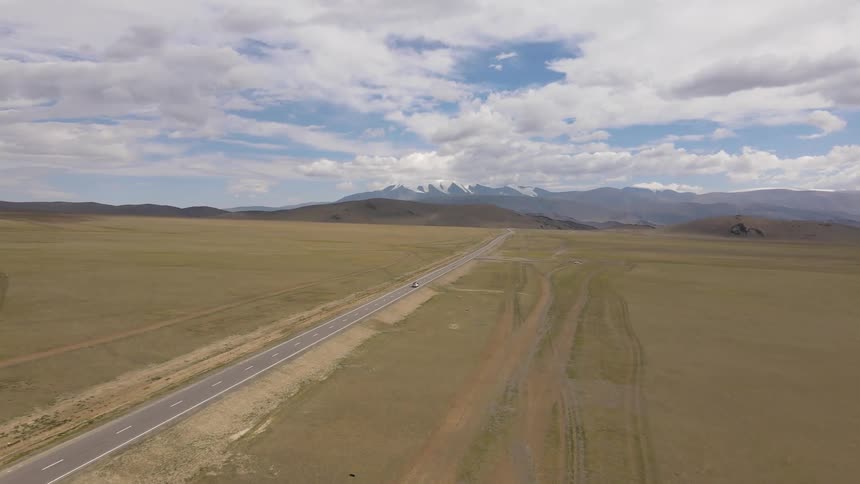 Aerial panorama of a road amid fields with mountains on the horizon