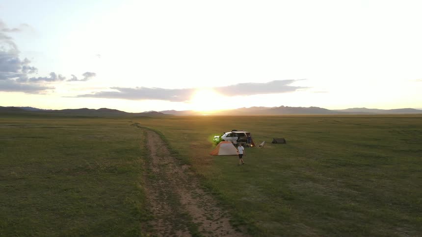 Three people are camping and taking photos in a remote grassland at sunset