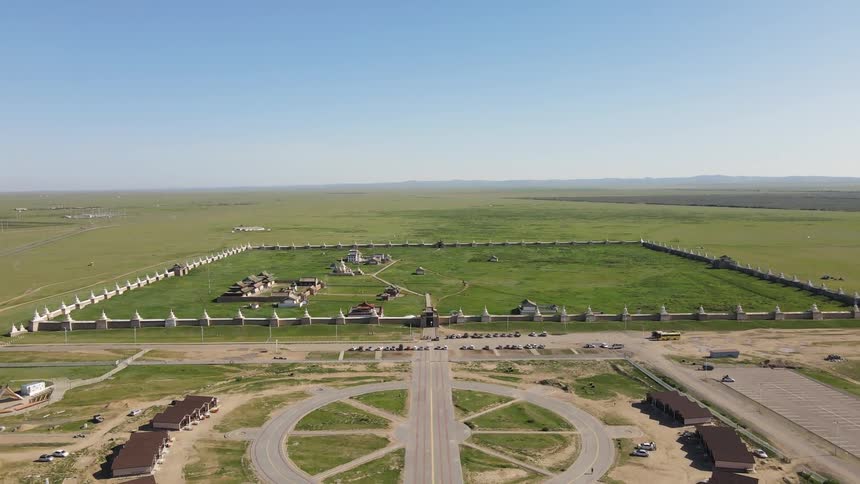 A symmetrical aerial view of a green field with a circular layout of structures and a road leading to it