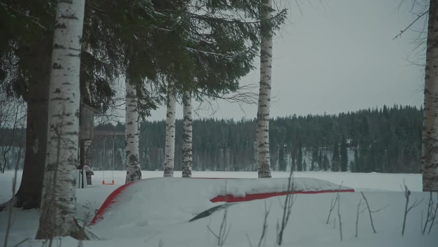 View of a small playground covered in snow with forests around on a cloudy day