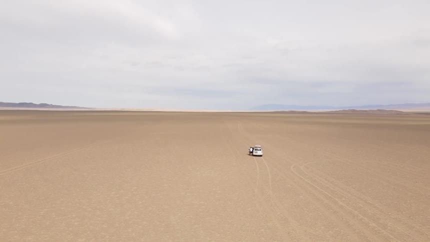 A white car is parked in the middle of the desert
