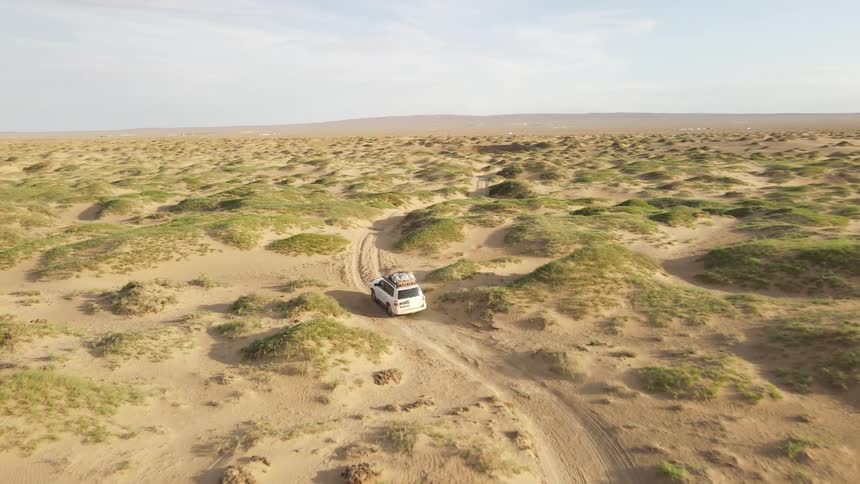 Vehicle drives along dirt road through arid hilly terrain