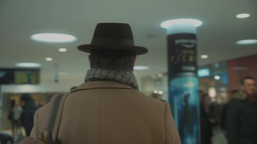 Man on a coat wearing a hat walk through the airport terminal