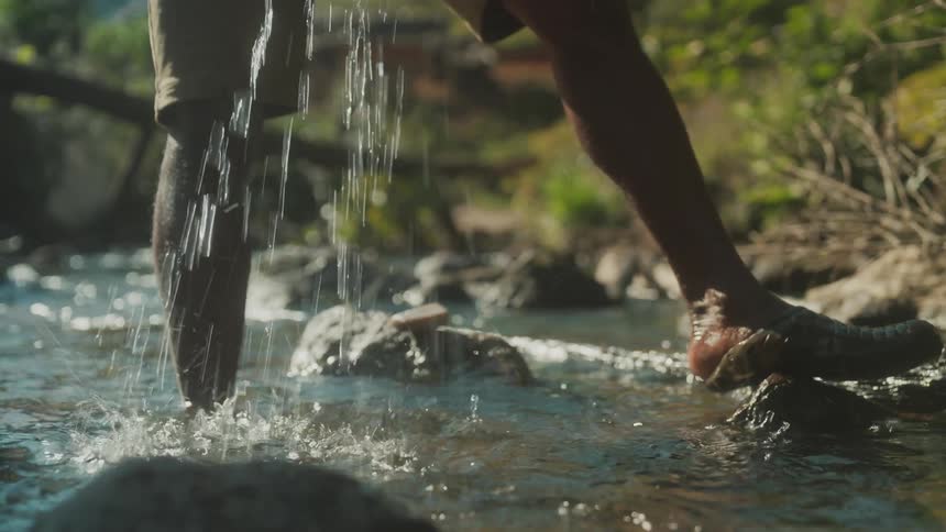 Closeup of a persons hands and legs washing a tshirt in the river