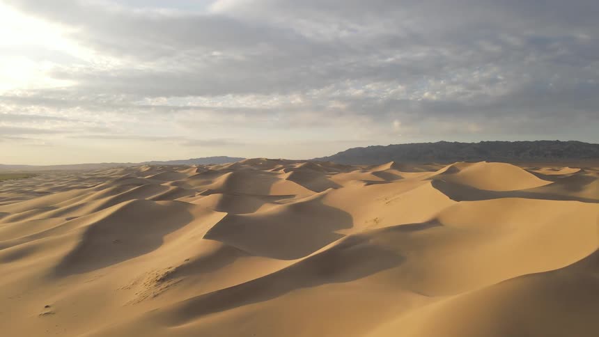 Sand dunes cast shadows into hollows of desert under an overcast sky