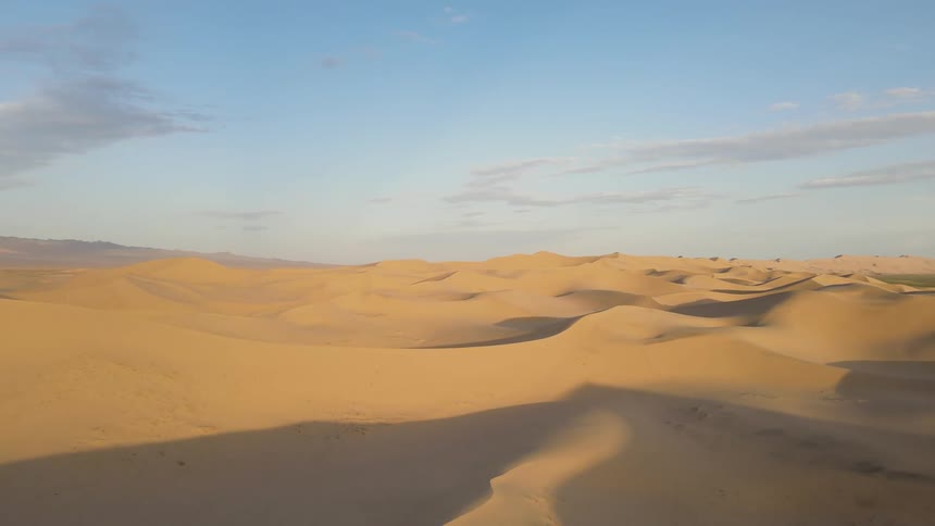 The sun shines brightly upon desert dunes with clouds in the sky