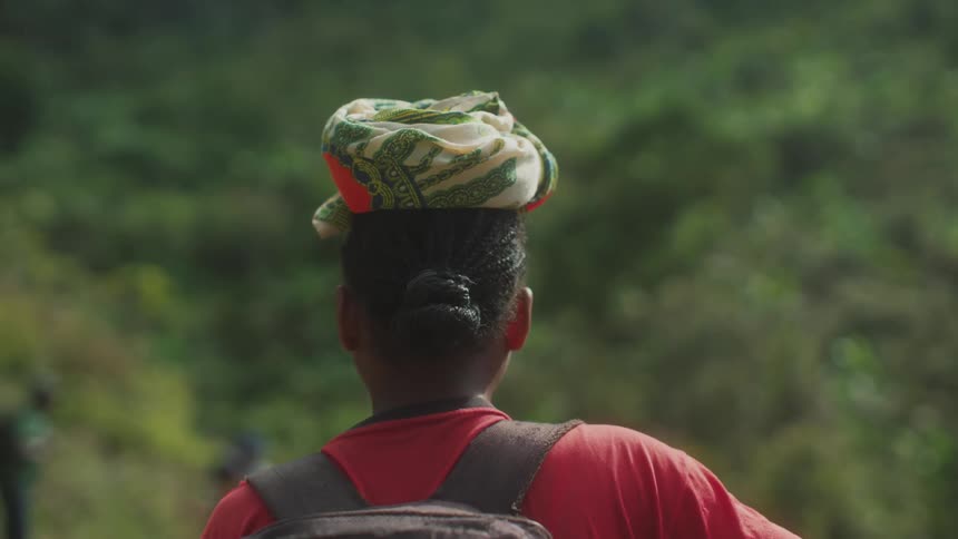 A woman carrying a backpack standing and watching others in the forest