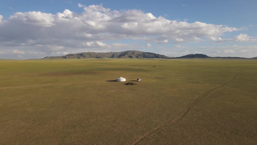 Aerial panorama of a tent in the midst of a grassland with a mountain range on the horizon
