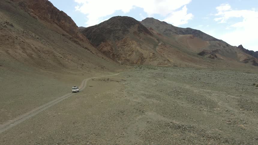 Aerial panorama of a car traveling on the ground beside a mountain range