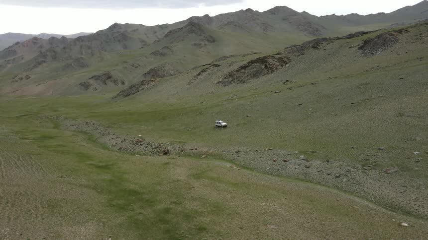 Vehicle sits parked in field between dry stream bed and mountains
