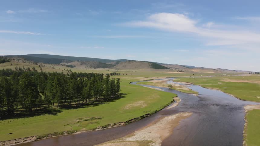 Aerial panorama of a central river amidst forests with mountain ranges in the horizon