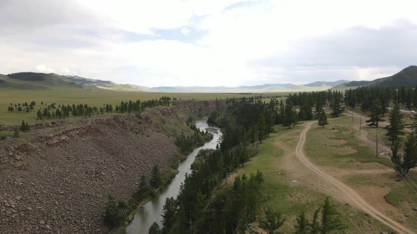 Trees and grassy plains line a river that runs through a canyon