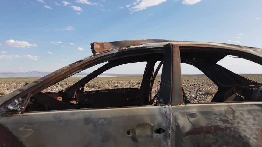 Rusted out and stripped car sits in desert with mountain on the horizon on a cloudy day