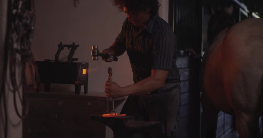 A man is forging a red hot steel with a hammer