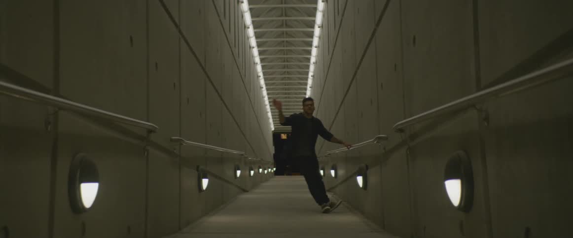 A man dances in a concrete hallway