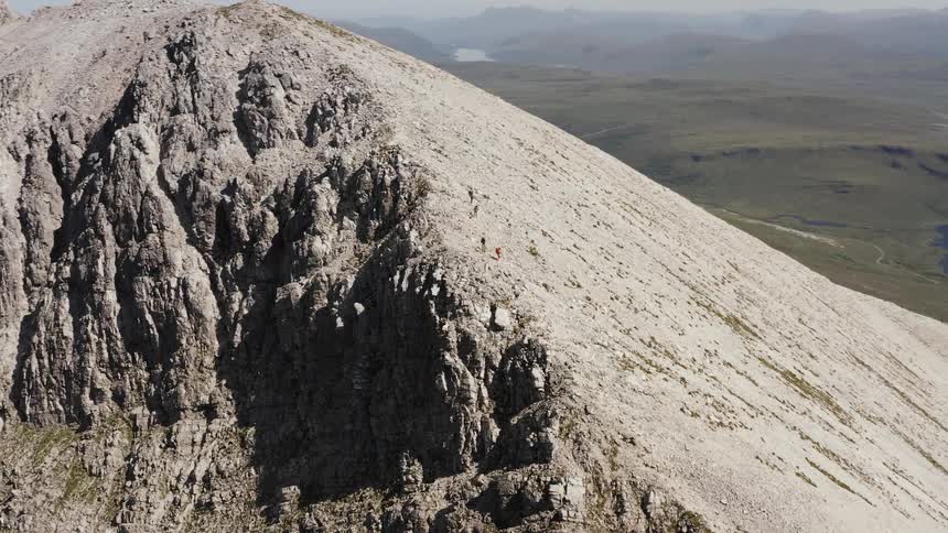 Aerial view around a rocky mountain peak with a sparsely green covered river valley and river in the background