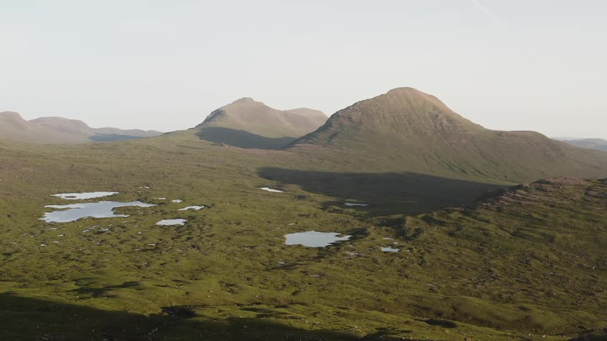 Mountains cast shadows across plain dotted with ponds on a foggy day