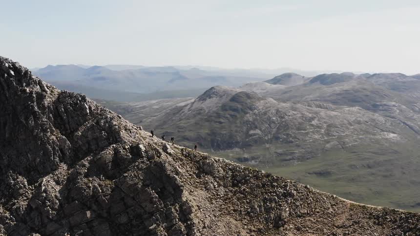 Aerial panorama of people hiking amidst a cliff under the mountains