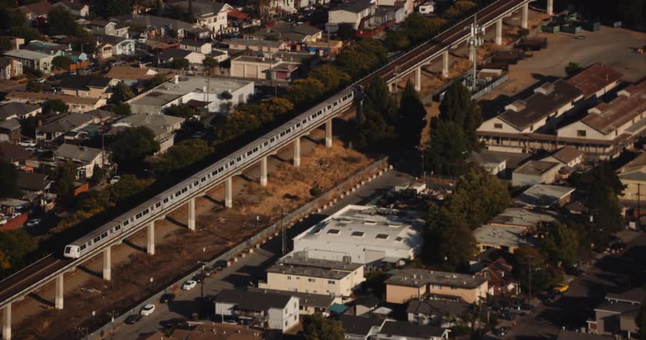 Passenger train moves along elevated tracks passing residential neighborhood, BART