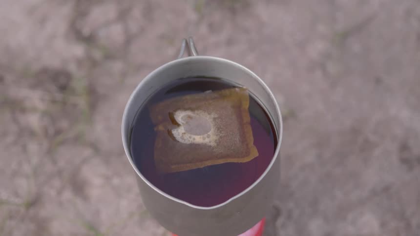 Bag of tea brewing in a tin cup