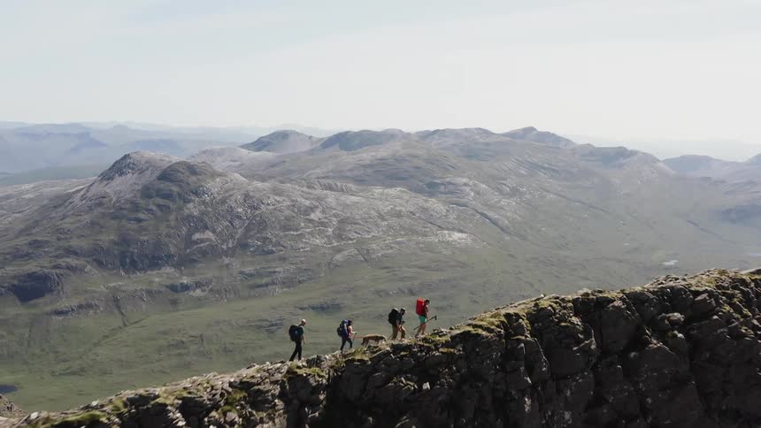 Mountaineers with a dog walking on the ridge of a mountain