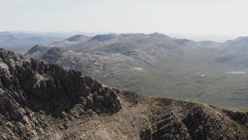 A sprawling valley is surrounded by rocky mountains under a hazy sky