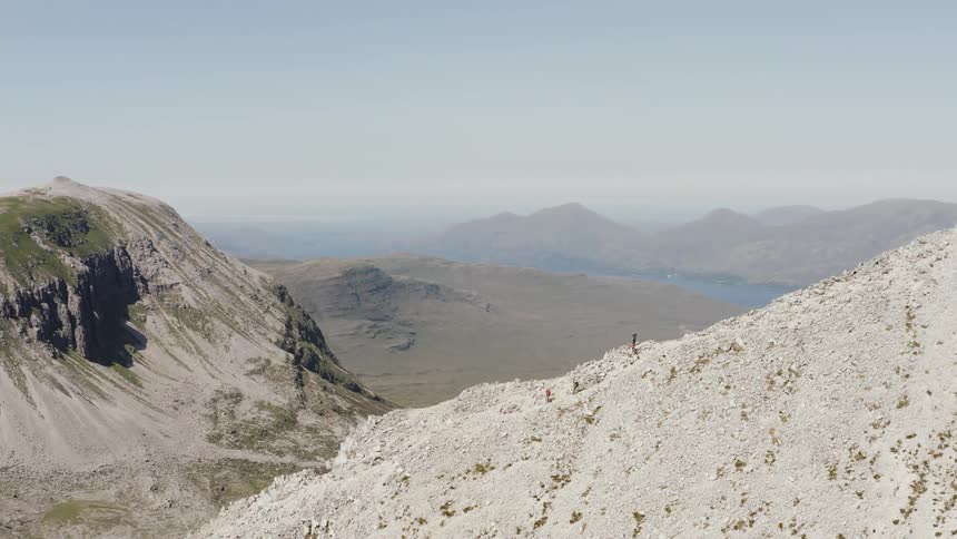 Small group of hikers walking along a barren white desert mountain ridge slope on a bright day