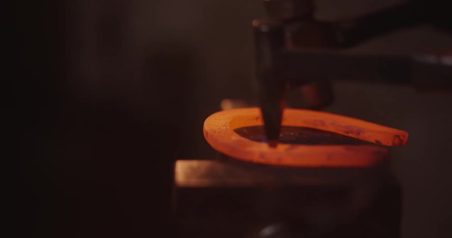 Blacksmith shaping a redhot horseshoe over an anvil
