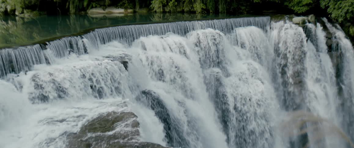 River water reflects nearby vegetation before flowing down wide falls