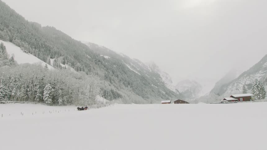 A sled is pulled off in the distance in a snow covered valley