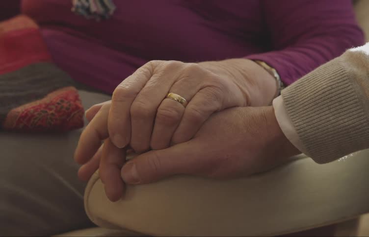 Older couple sits together holding hands