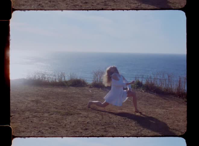 A woman on the coastline is wearing a white shirt and dancing