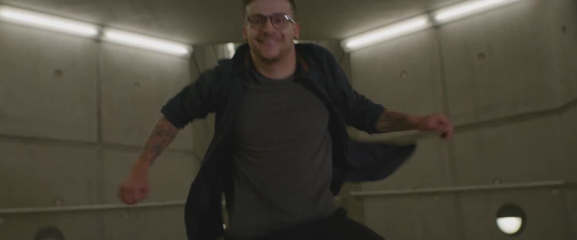 A man dances in a concrete corridor