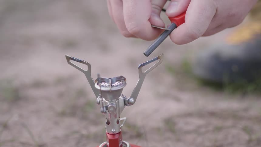 Closeup of a persons hands generating sparks with a tool towards a portable stove