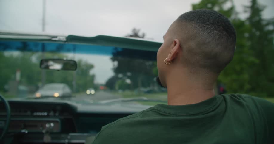 Young man sitting on a car driving through the neighborhood