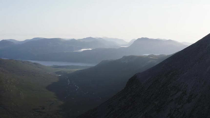 Silhouette of a hillside blocking the sun and a river valley with fog covered mountains in the background
