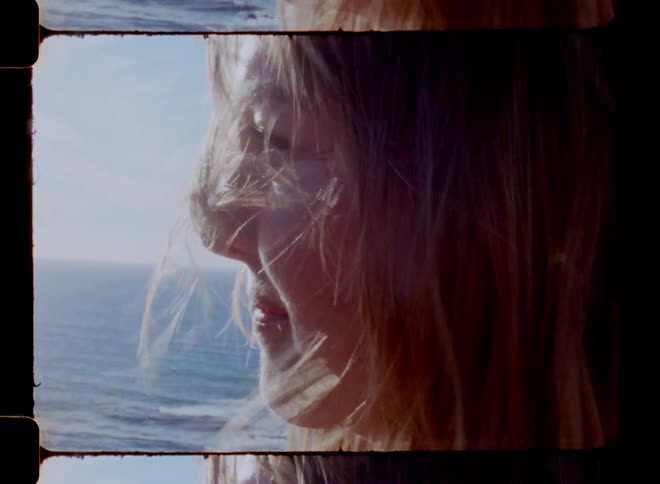 Woman stares out to sea as wind blows her hair across her face