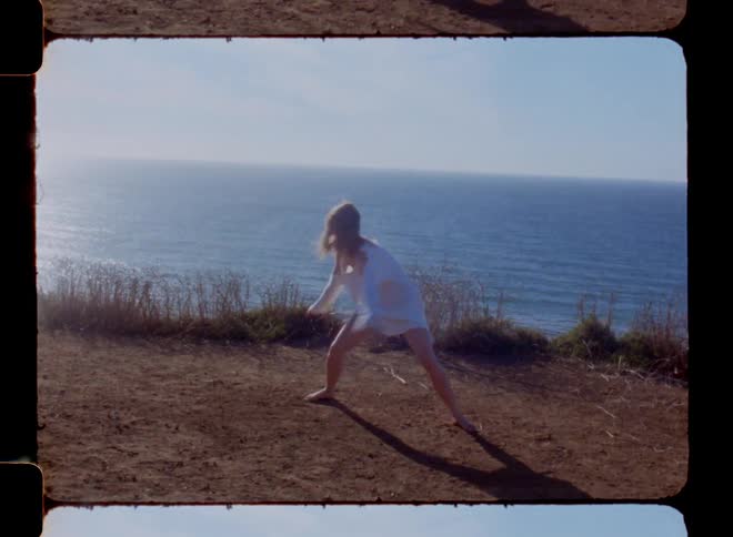 Woman on a white dress dances next to the ocean