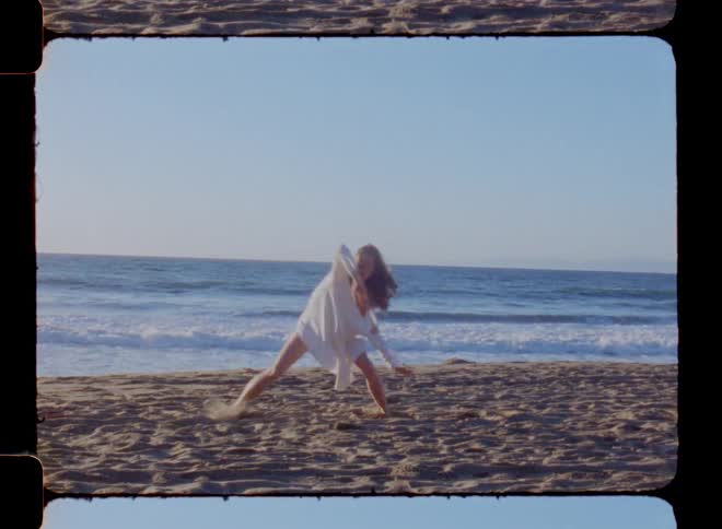 A woman in a while dress dances on a sandy beach on a sunny day