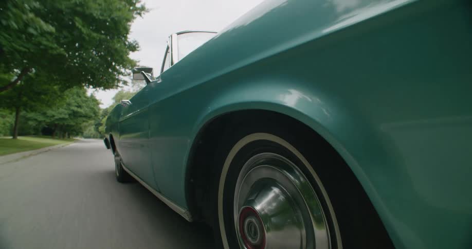 Front wheel side profile of light blue fifties hotrod convertible driving down an empty road