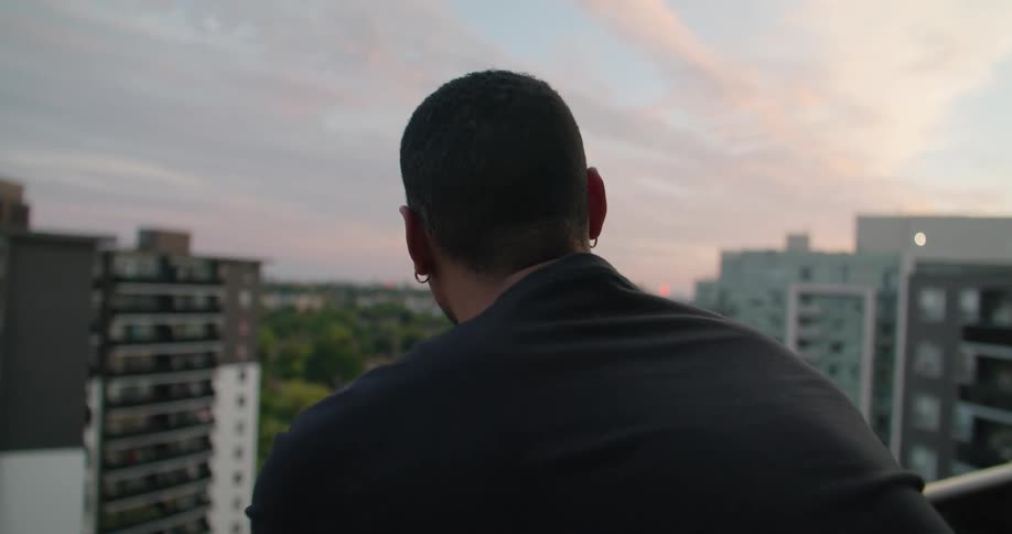 Back of a man looking at the city from a balcony at sunset