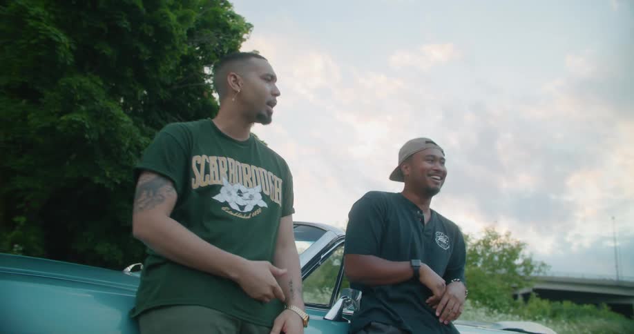 Two friends talking leaning against a parked car