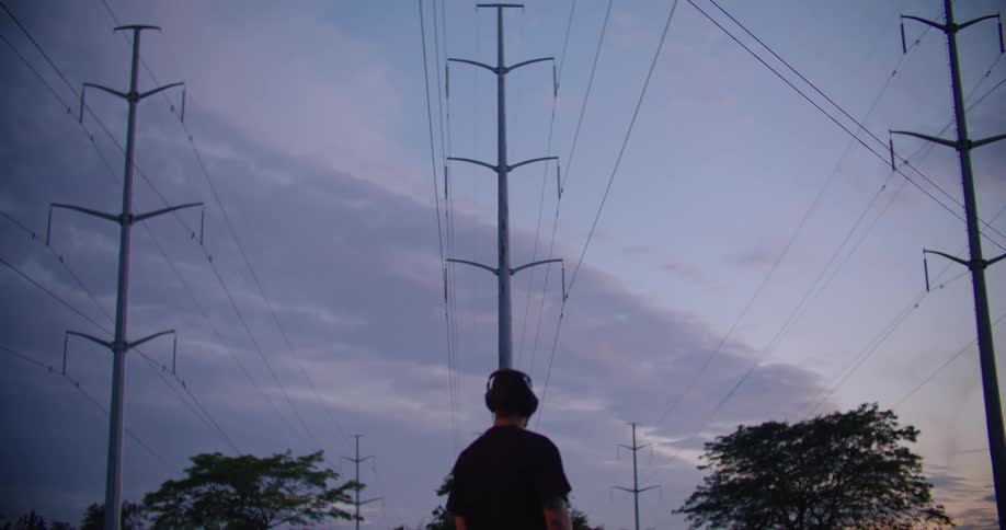 Man with his back turned wearing headphones under a morning sky