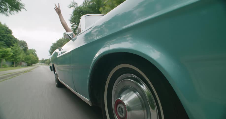 A person enjoying a ride in a vintage blue convertible making a sign with their hand
