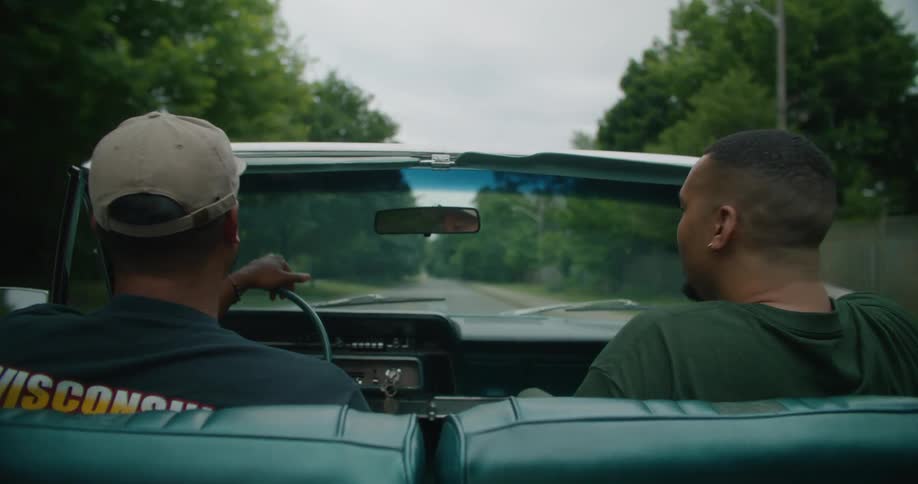View of two men sitting in a convertible clapping their hands while driving on a treelined street