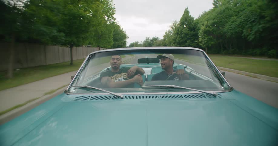 Two men in a car shaking hands as thy drive down the road