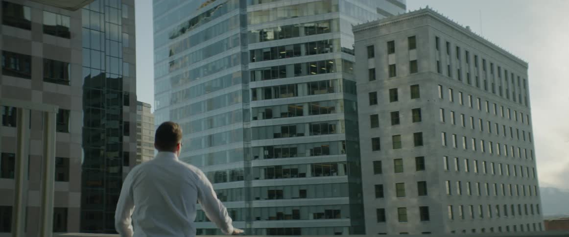 A man walks onto a balcony surrounded by large city buildings
