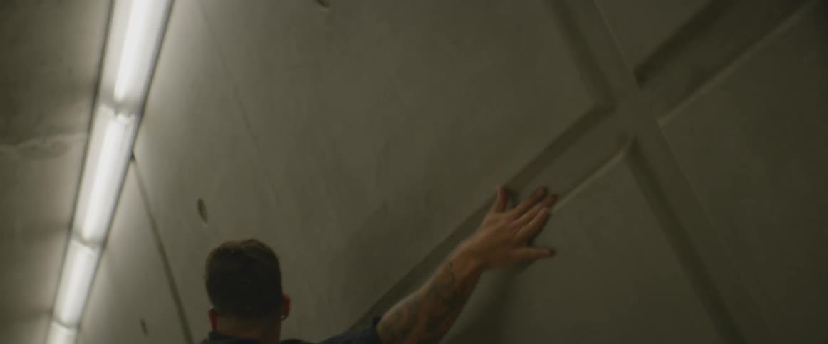 Man dances and runs his hand against grey concrete wall